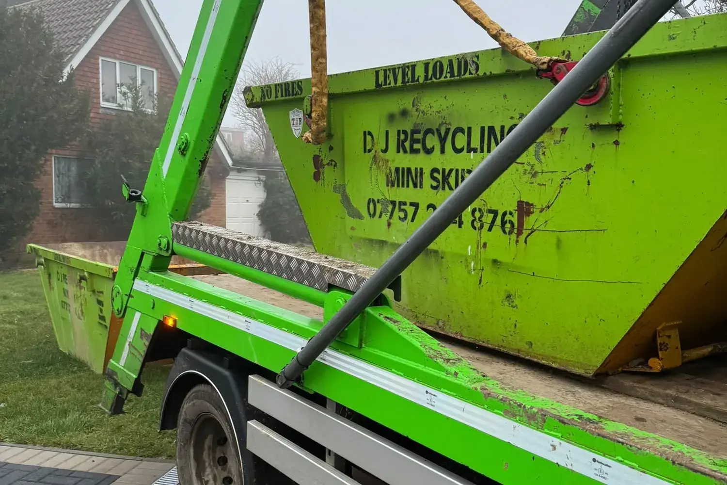 DJ Recycling skip lorry placing a mini skip on a front garden